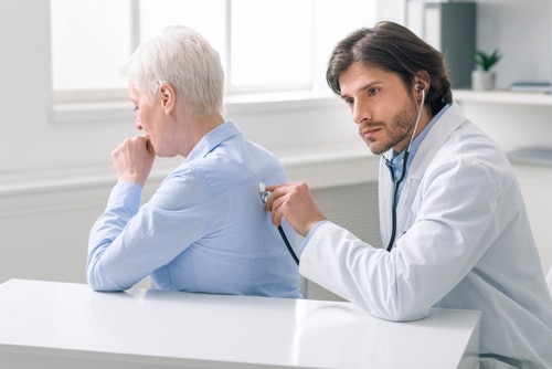 Serious doctor listening to coughing senior patient
