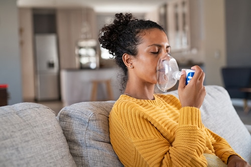 Black woman holding a mask nebulizer inhaling fumes medication into lungs.