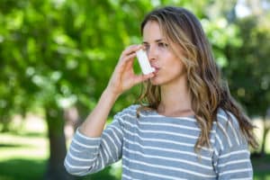 Woman using asthma inhaler in a park